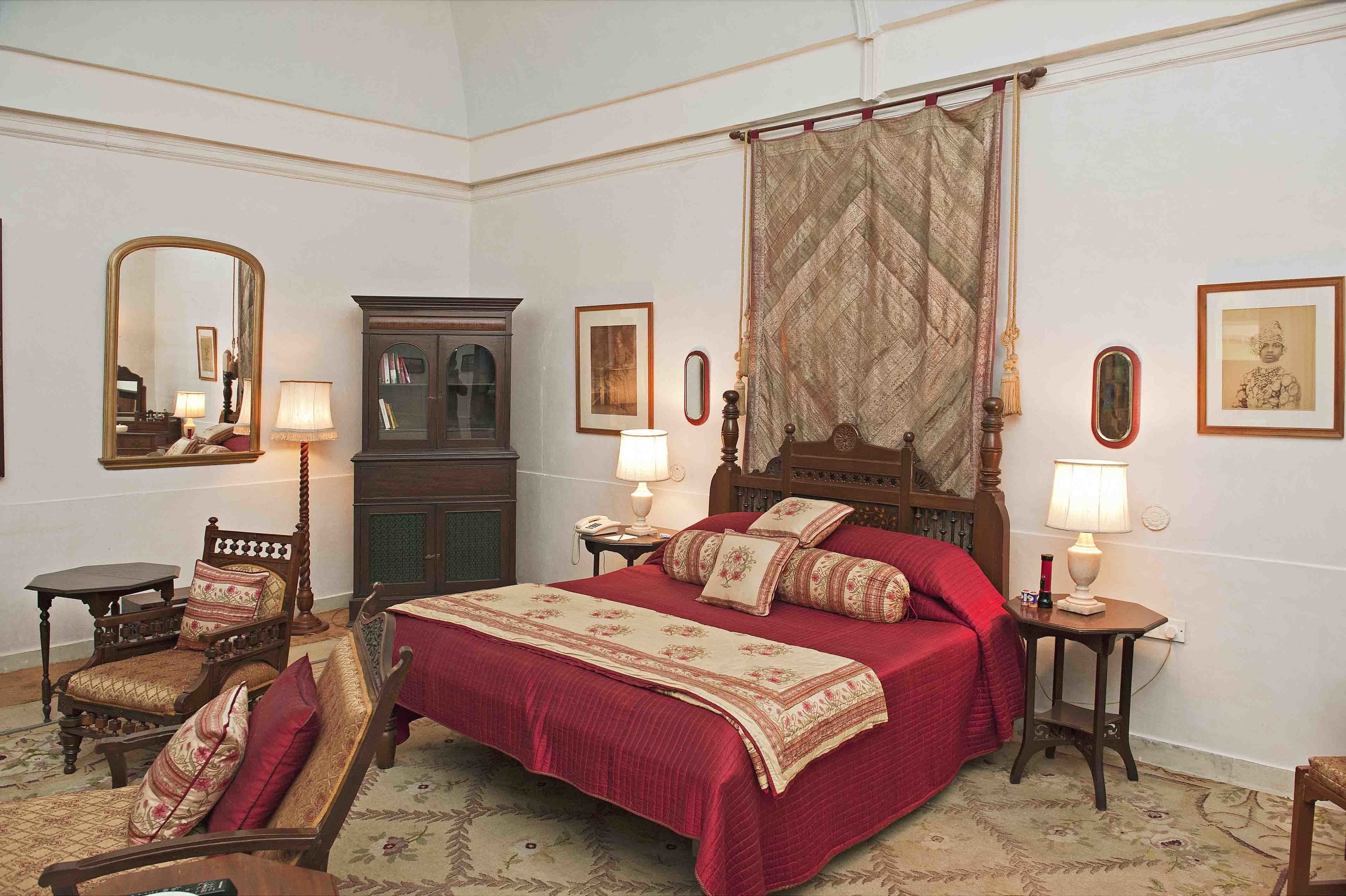 A traditional bedroom with a large bed, two bedside tables with lamps, a wooden chair, a cabinet, and a mirror.