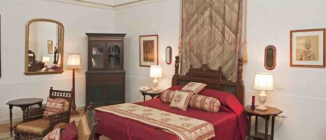 Une chambre à coucher de style traditionnel, avec un grand lit, deux tables de chevet avec des lampes, une chaise en bois, une armoire et un miroir.