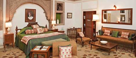 Una habitación tradicional con cama, sofá y una pequeña mesa. Hay un espejo en la pared y un cuadro sobre la cama.