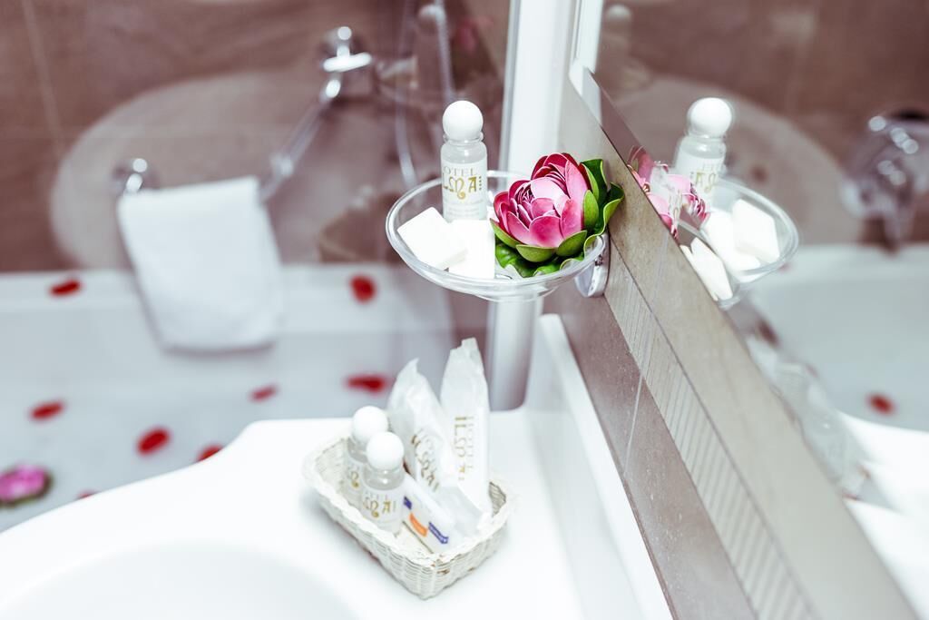 A bathroom with a mirror, toiletries, and a decorative pink flower.