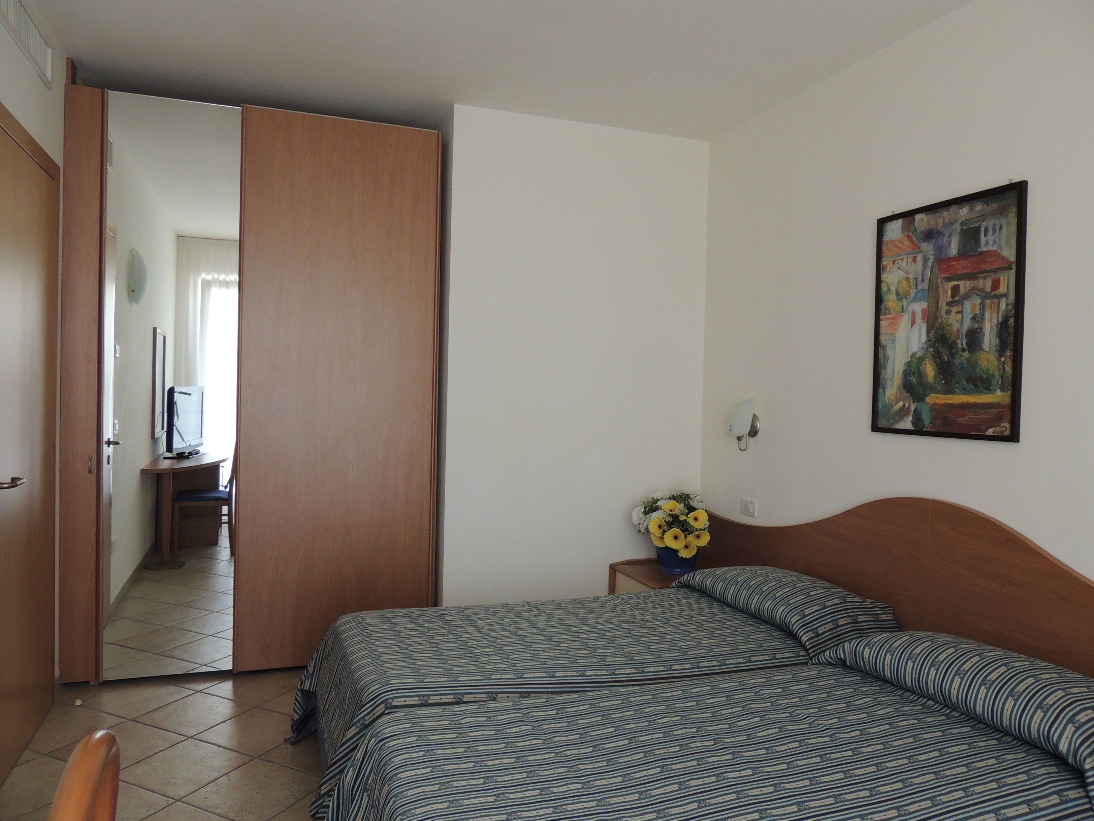A bedroom with a bed, a desk, a chair, a TV, and a painting on the wall.