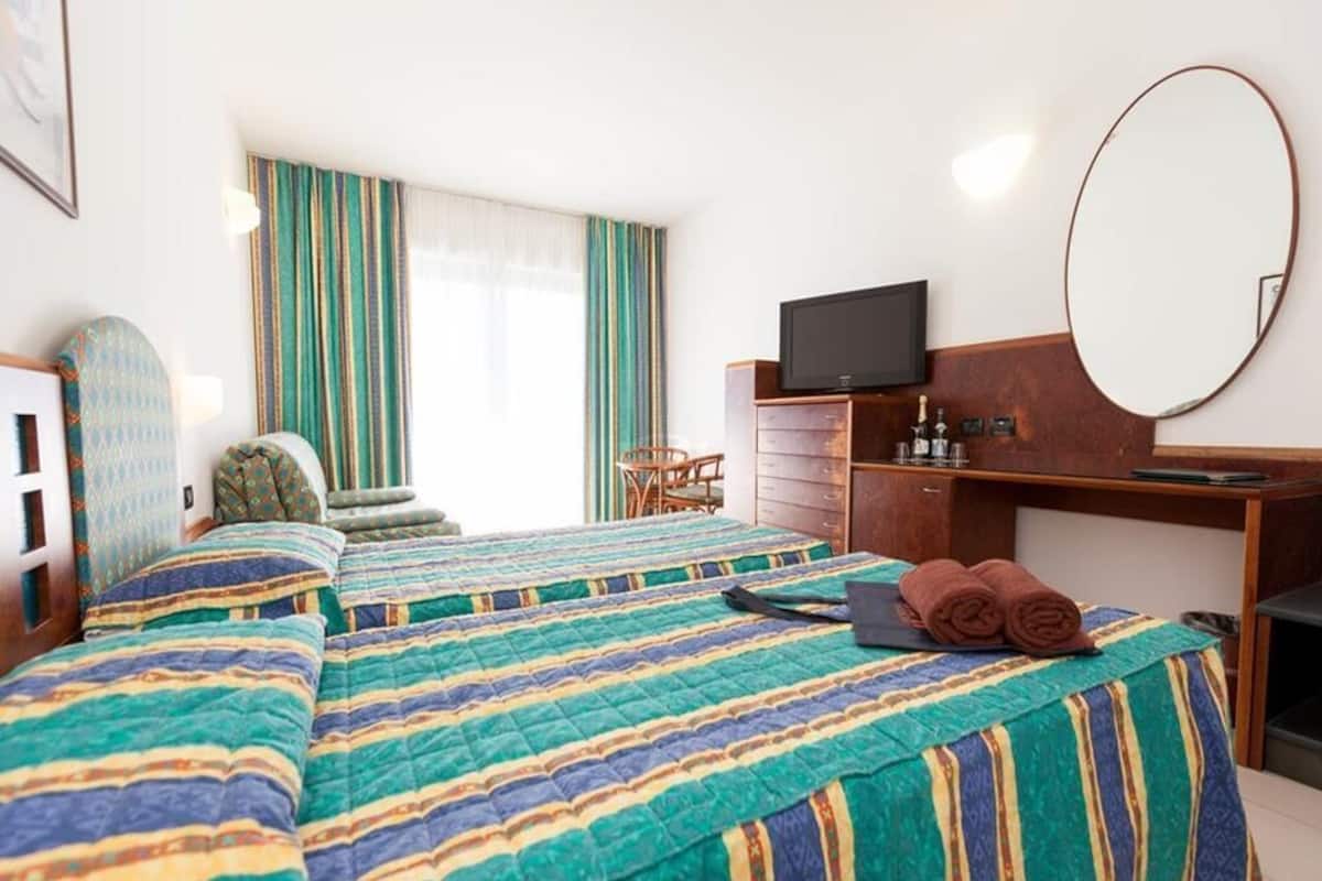 A hotel room with two beds, a desk, a television, and a large mirror.