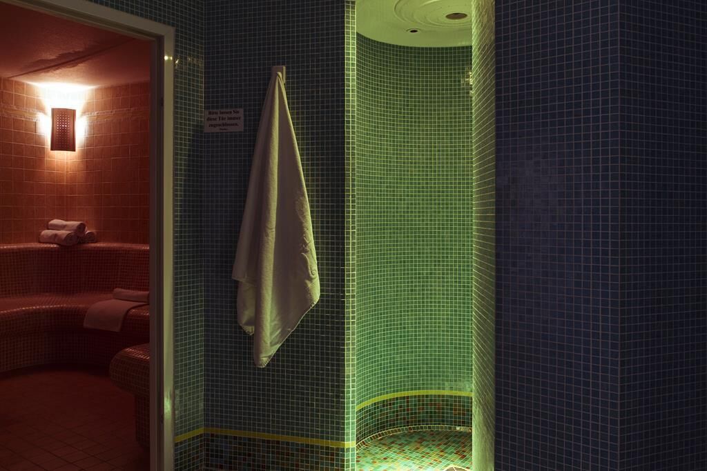 Un baño con cabina de ducha con azulejos verdes, una toalla colgada en la pared y una señal visible.