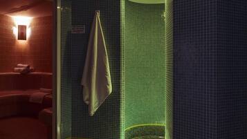 Un baño con cabina de ducha con azulejos verdes, una toalla colgada en la pared y una señal visible.