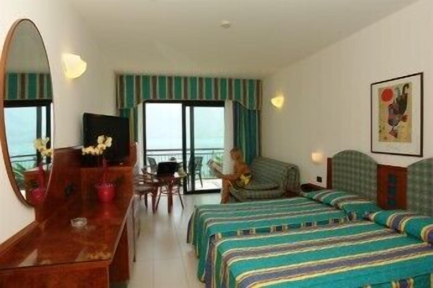 Habitación de hotel con cama, escritorio, silla, televisor y vista al océano.