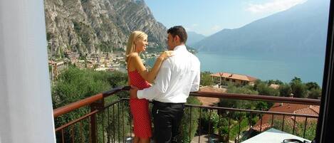 A couple on a balcony overlooking a mountainous landscape with a lake and buildings.