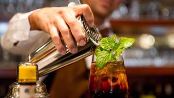 A bartender pouring a drink into a glass with ice and a mint garnish.