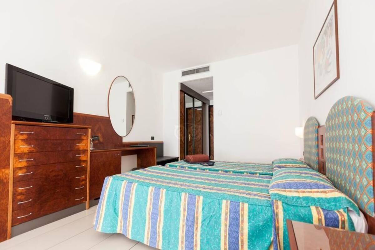 A hotel room with a wooden dresser, a television, a bed with patterned bedding, and a mirror.