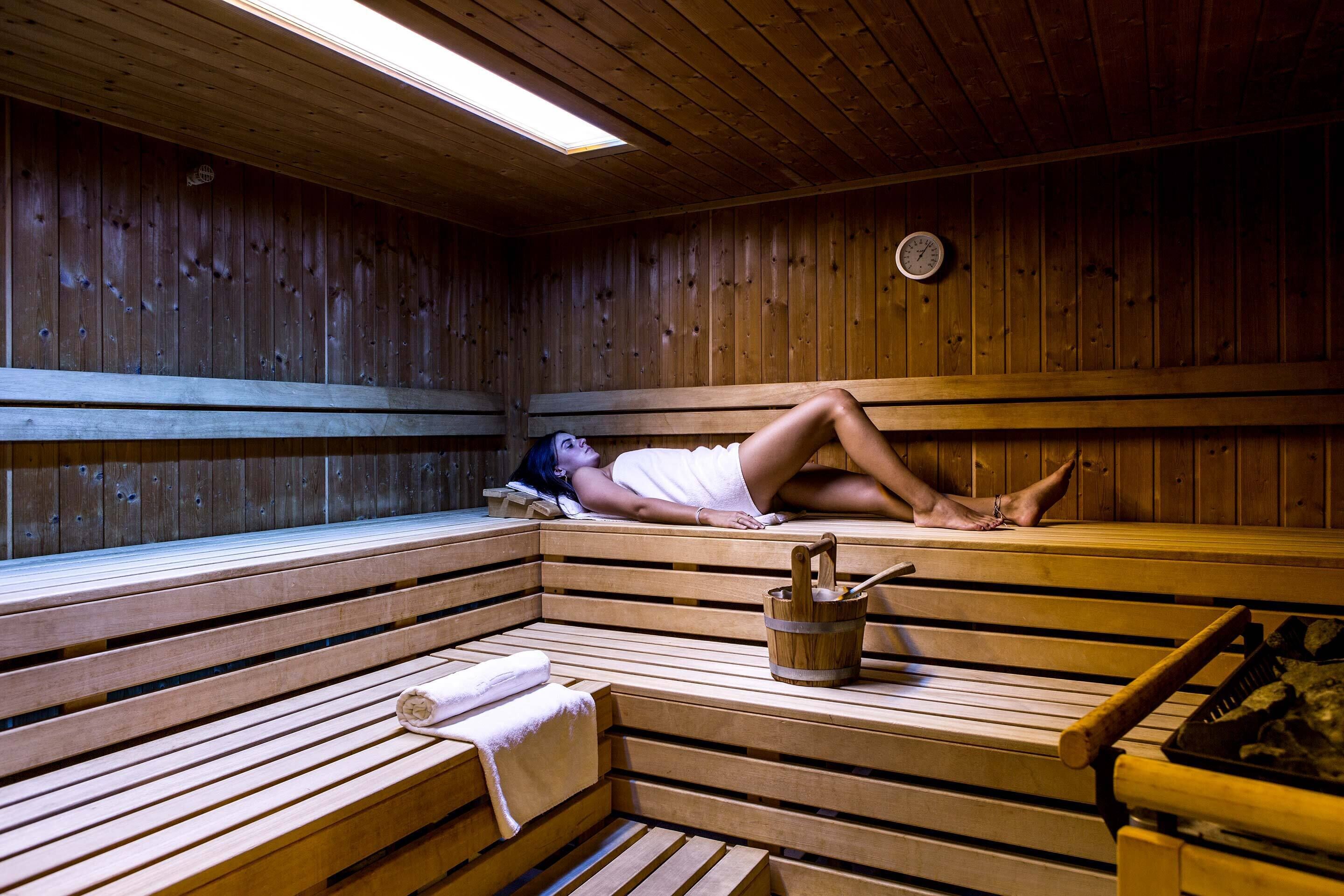 Una sauna con bancos de madera, un reloj en la pared y un cubo con un cepillo.