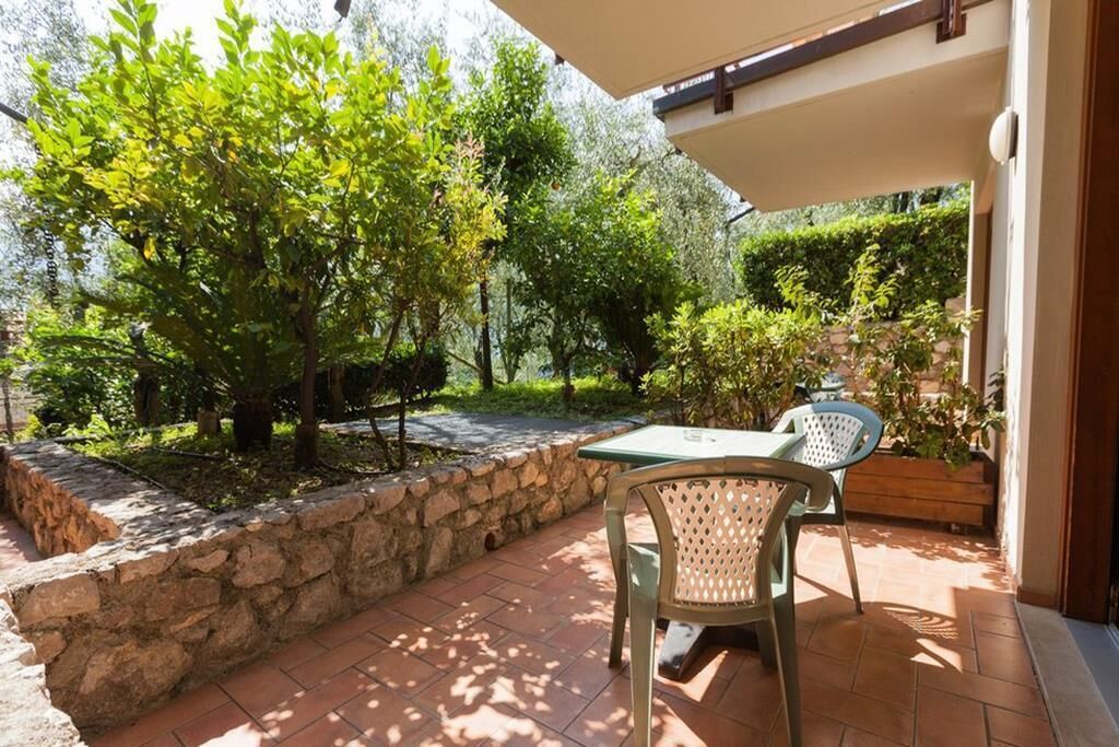 Un patio al aire libre con una mesa y sillas, rodeado de muros de piedra y follaje.