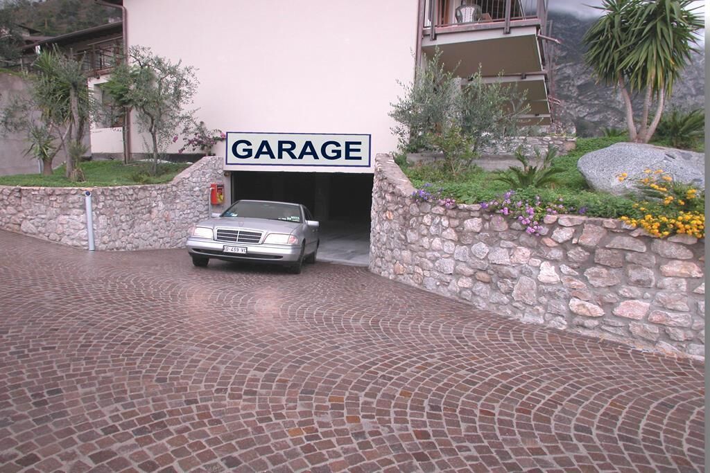 A garage entrance with a car parked inside, surrounded by a stone wall and a paved driveway.