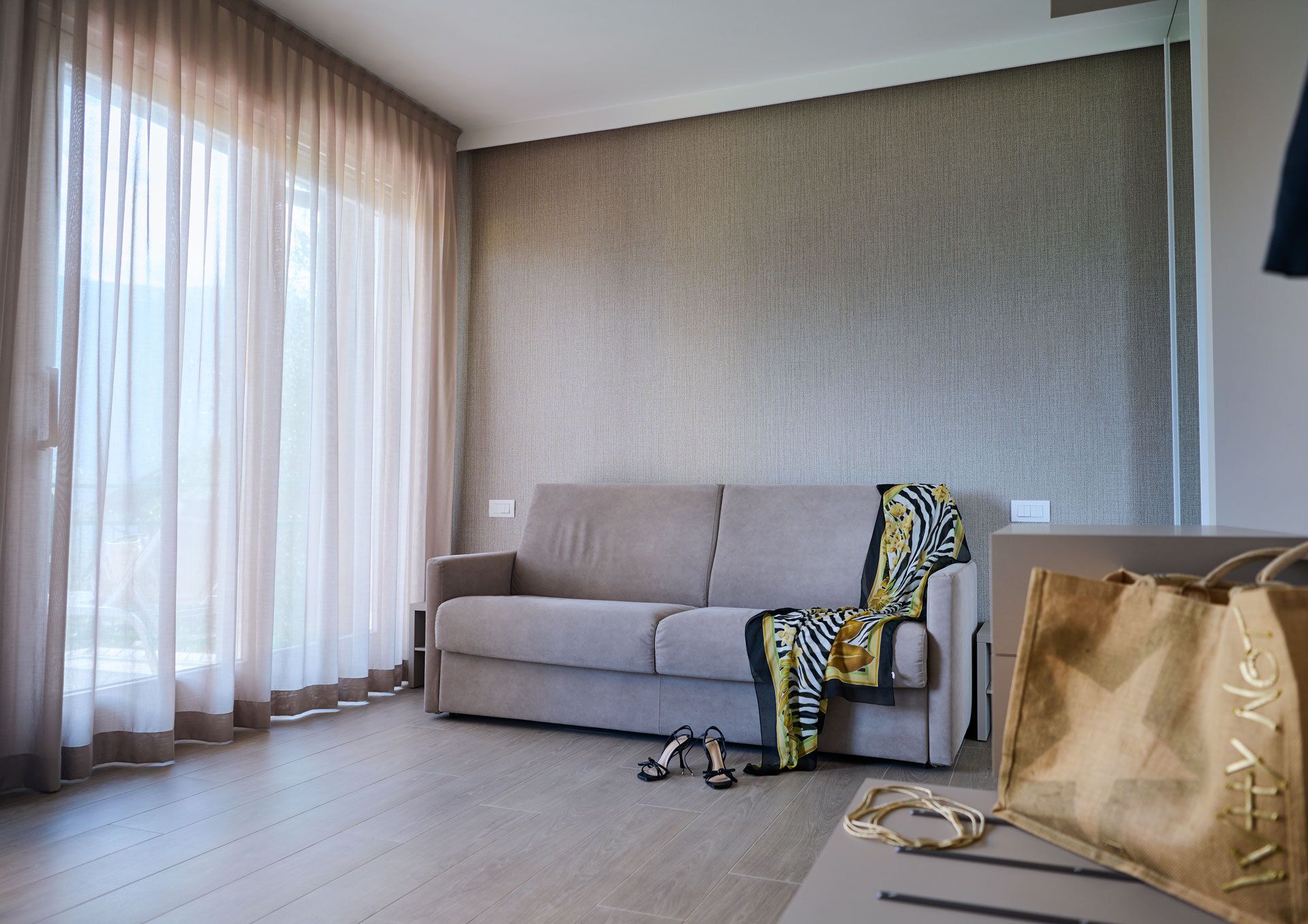 A modern living room with a beige sofa, a zebra-patterned throw, and a large window with sheer curtains.