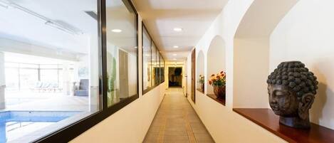 A corridor with a pool view, a Buddha statue, and a tiled floor.