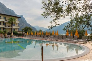 Un espace piscine doté de chaises longues et de parasols, entouré de montagnes et d’un bâtiment d’hôtel.