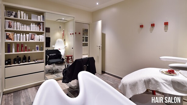 Un salón de belleza con una decoración moderna, que incluye una zona de recepción, estanterías con productos para el cabello, una silla de peluquería y una mesa para tratamientos.