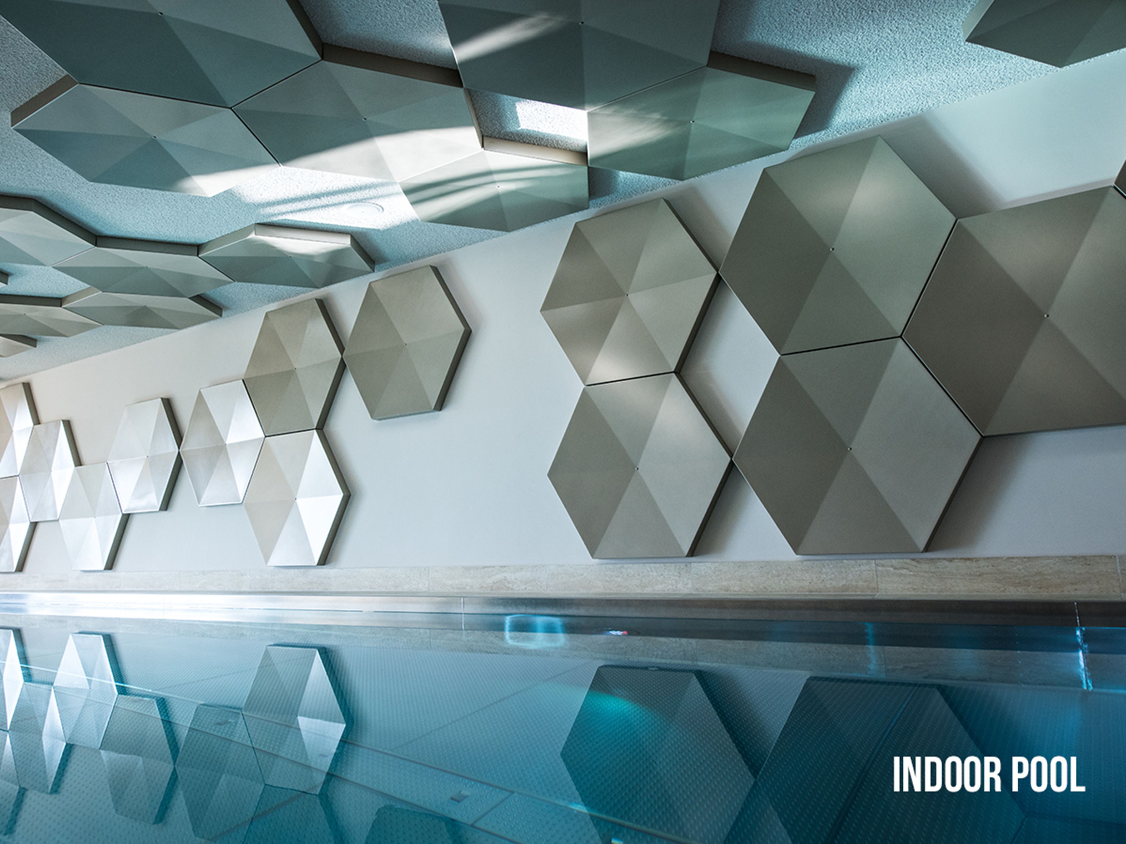 A modern indoor pool with geometric wall panels and a clear glass floor.