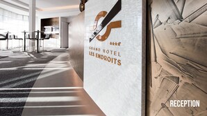 A modern hotel reception area with a large logo, a reception desk, and a seating area with tables and chairs. - Grand Hôtel Les Endroits (La Chaux-de-Fonds)