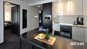 A modern kitchen with a glass dining table, a coffee machine, and a built-in dishwasher. - Grand Hôtel Les Endroits (La Chaux-de-Fonds)