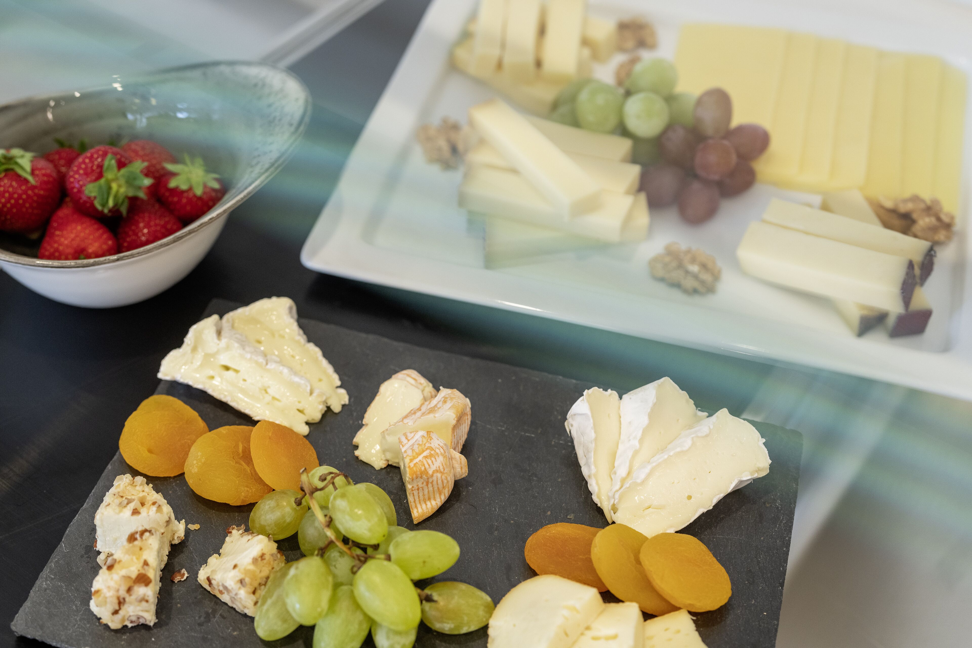 Une sélection de fromages, de raisins et d’abricots présentés sur une planche d’ardoise.