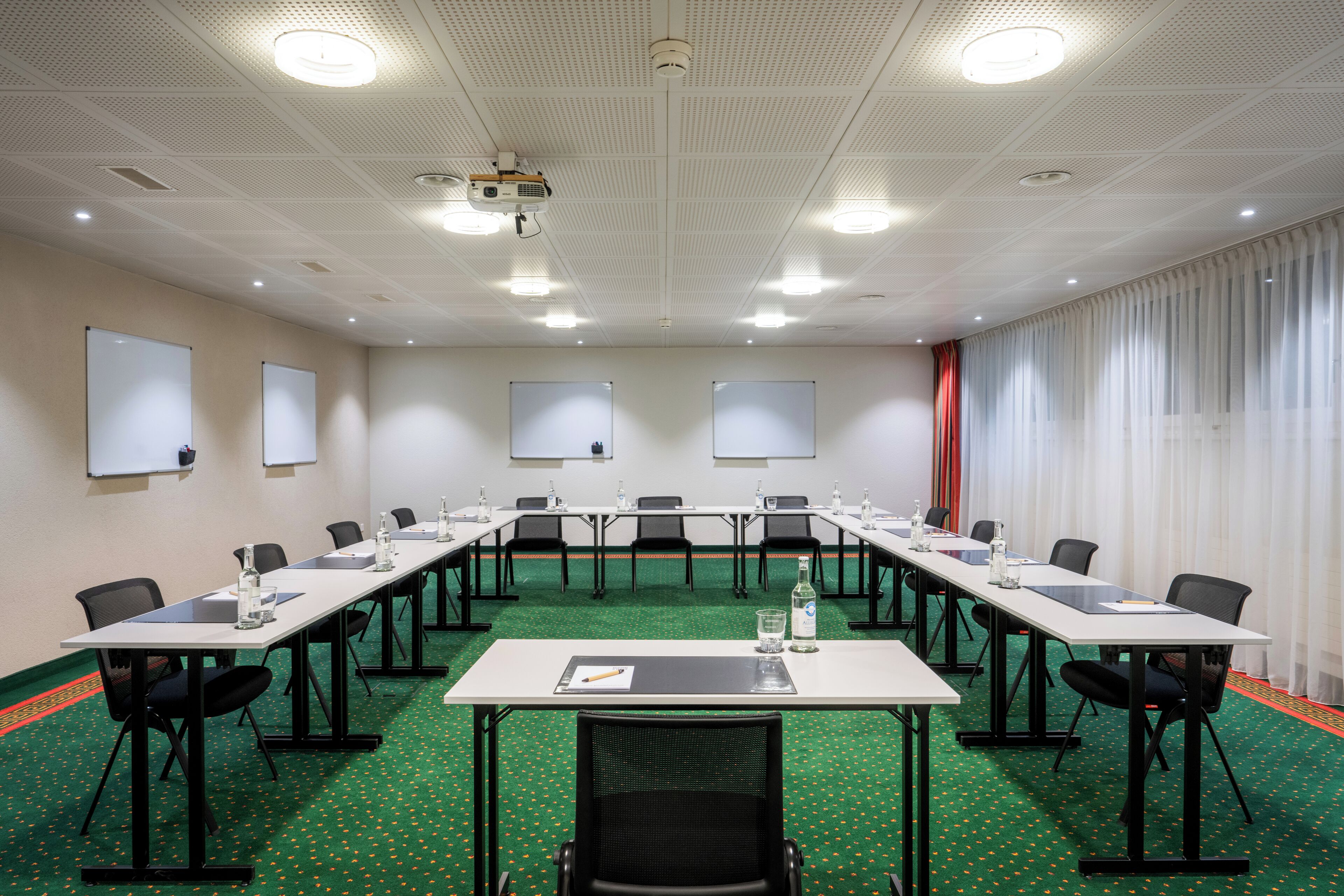 Une salle de conférence équipée d’une longue table, de chaises, d’un projecteur et d’un tableau blanc.