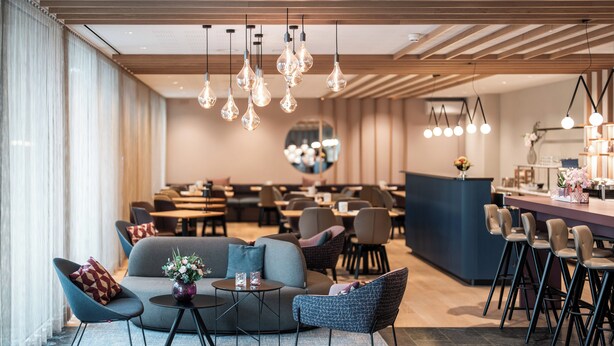 A modern hotel lobby with seating areas, a bar, and a large mirror.