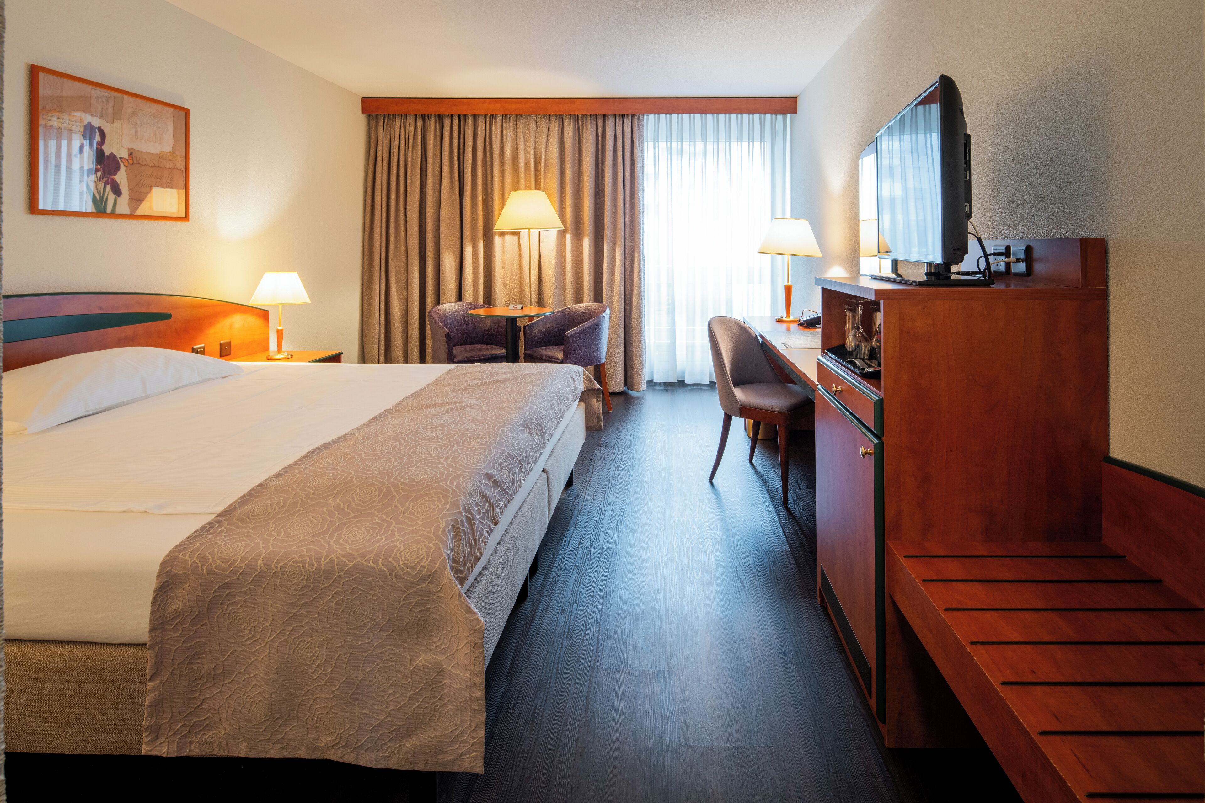 Una habitación de hotel con una cama grande, un escritorio, una silla, un televisor y una ventana con cortinas.