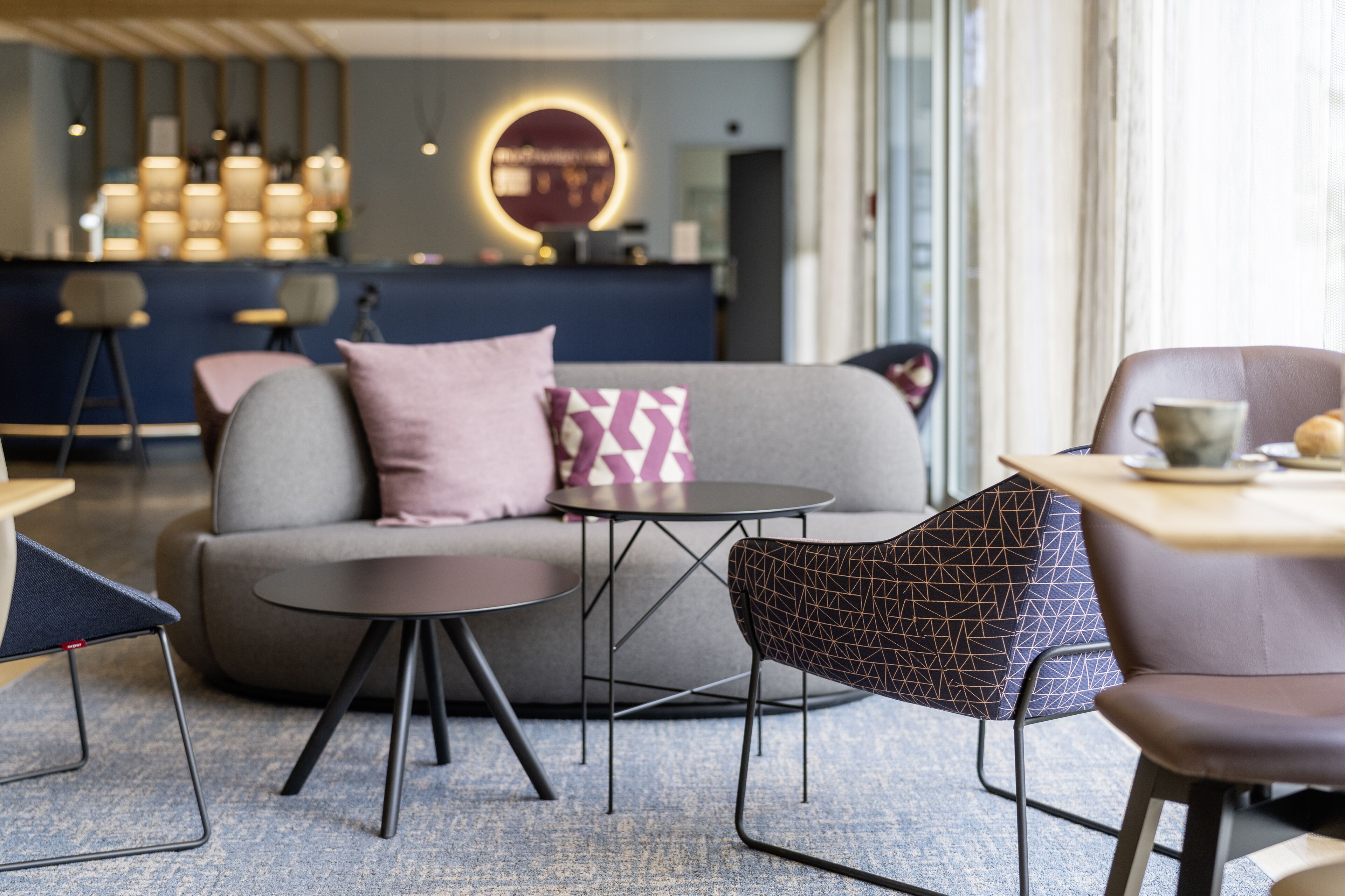 A modern lounge area with a sofa, round tables, and patterned chairs.