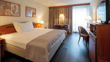 A hotel room with a large bed, a desk with a chair, a television, and two lamps.
