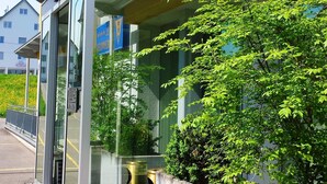 A modern building with a glass entrance, a covered walkway, and a well-maintained garden area.