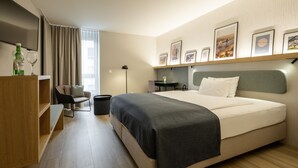A modern hotel room with a large bed, a desk, a chair, and a TV.