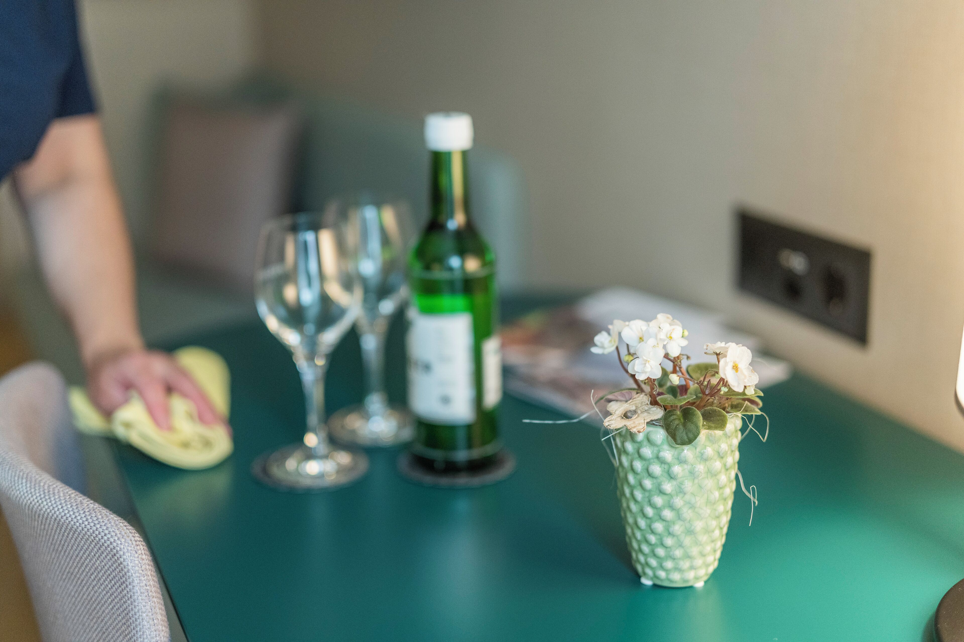 Une table avec une bouteille verte, des verres à vin et un petit vase avec des fleurs.
