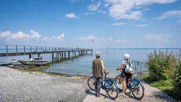 Une scène côtière avec une jetée s’avançant dans des eaux calmes, deux vélos garés sur un sentier et un ciel dégagé.