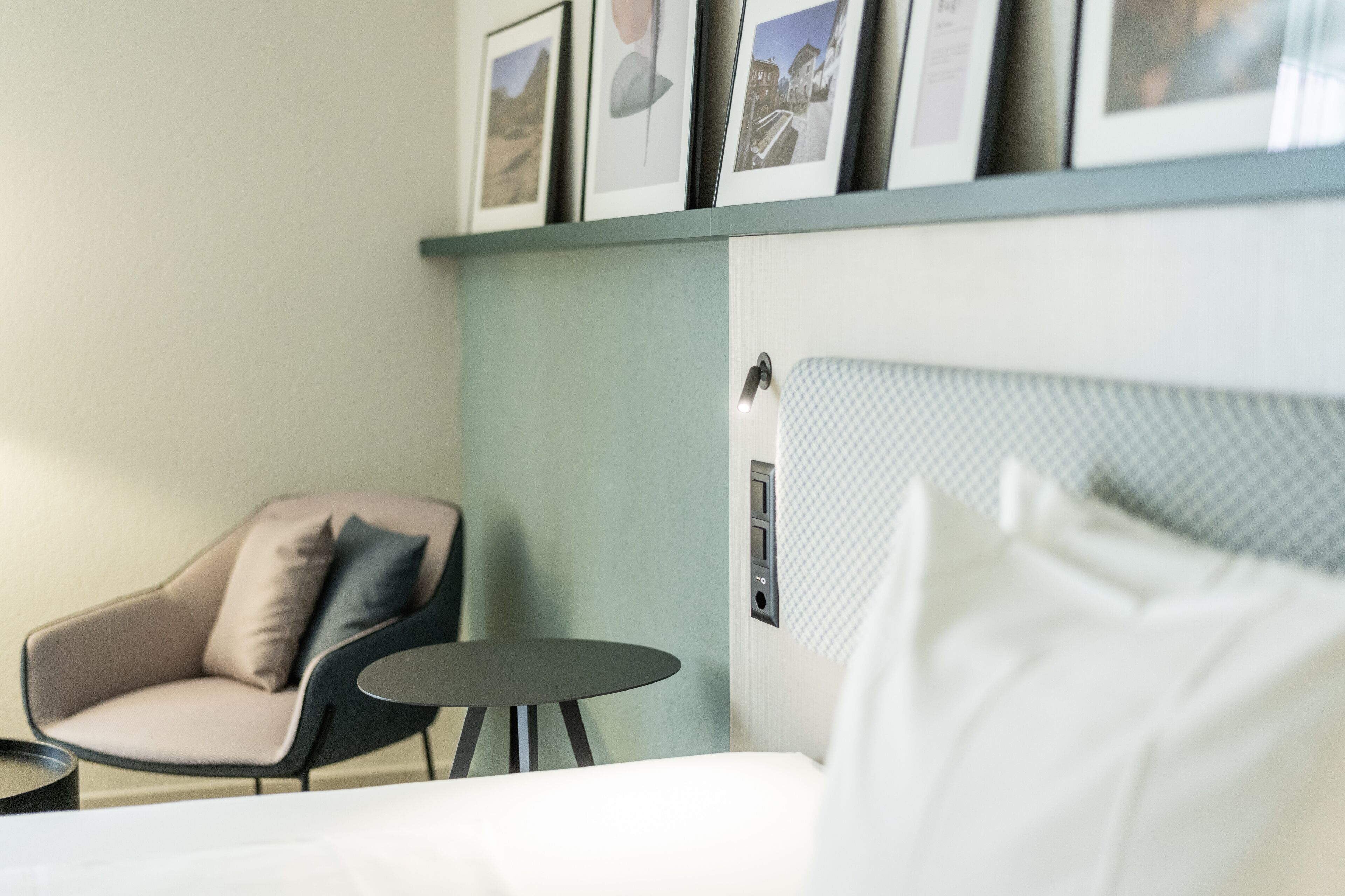 Una habitación de hotel con cama, una silla, una mesita y cuadros en la pared.