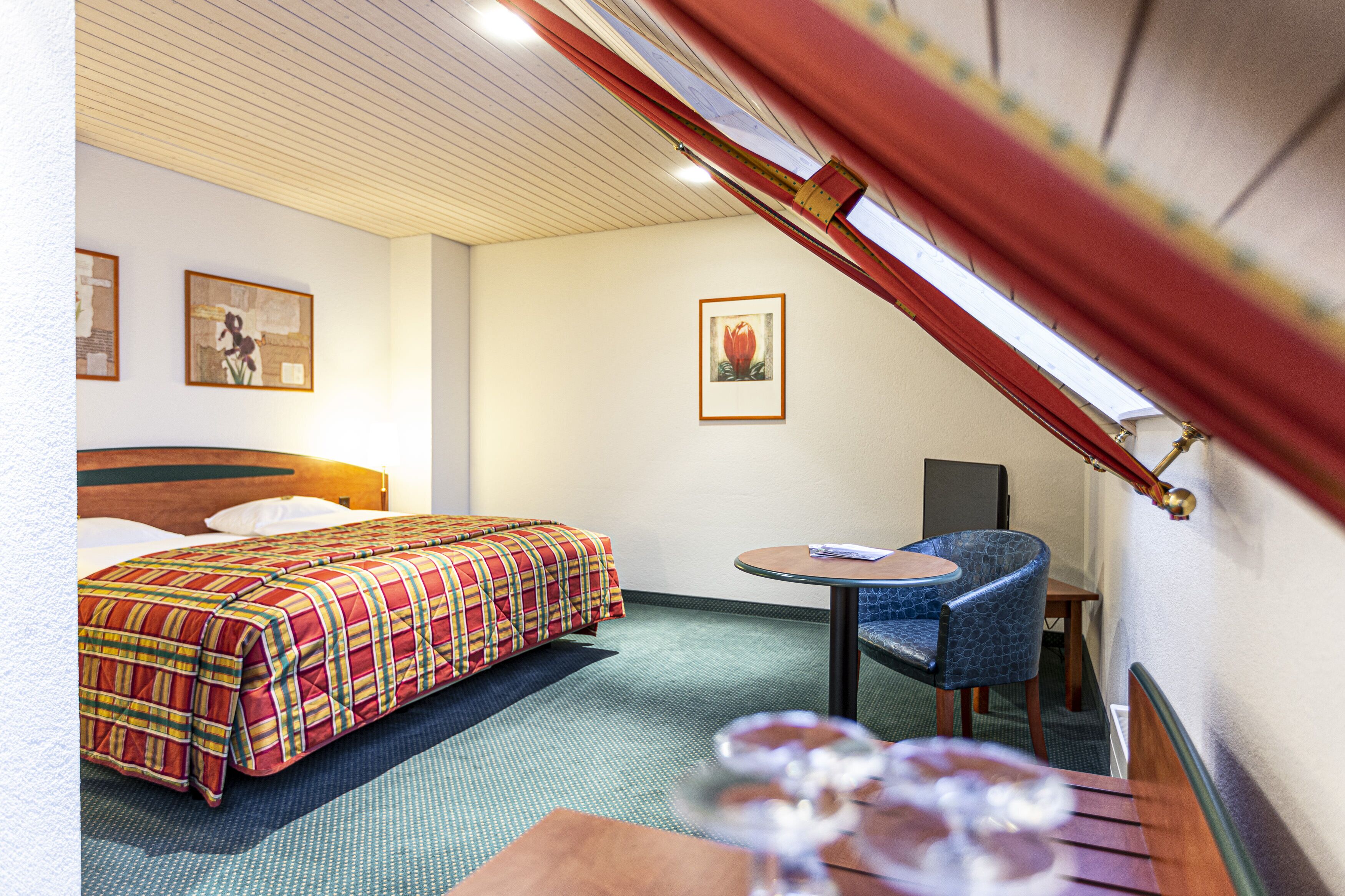 Une chambre d’hôtel avec un lit, une petite table, une chaise et un tableau au mur.
