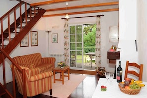 Una sala de estar acogedora con una escalera de madera, un sofá a rayas, una mesita con un jarrón y un comedor con una mesa dispuesta para dos.