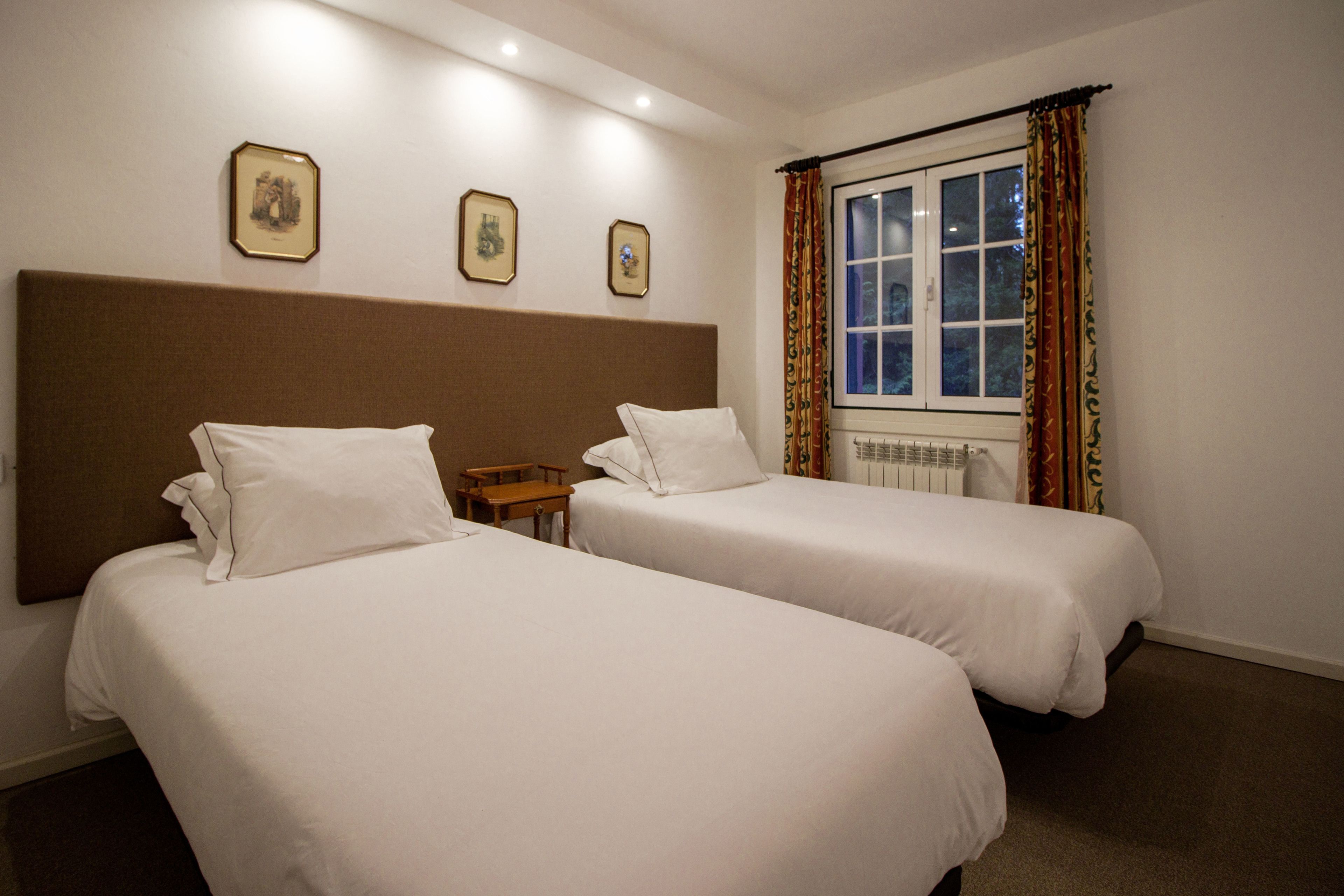 A hotel room with two single beds, a wooden nightstand, and a window with curtains.