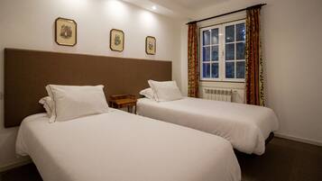 Una habitación de hotel con dos camas individuales, una mesita de noche de madera y una ventana con cortinas.