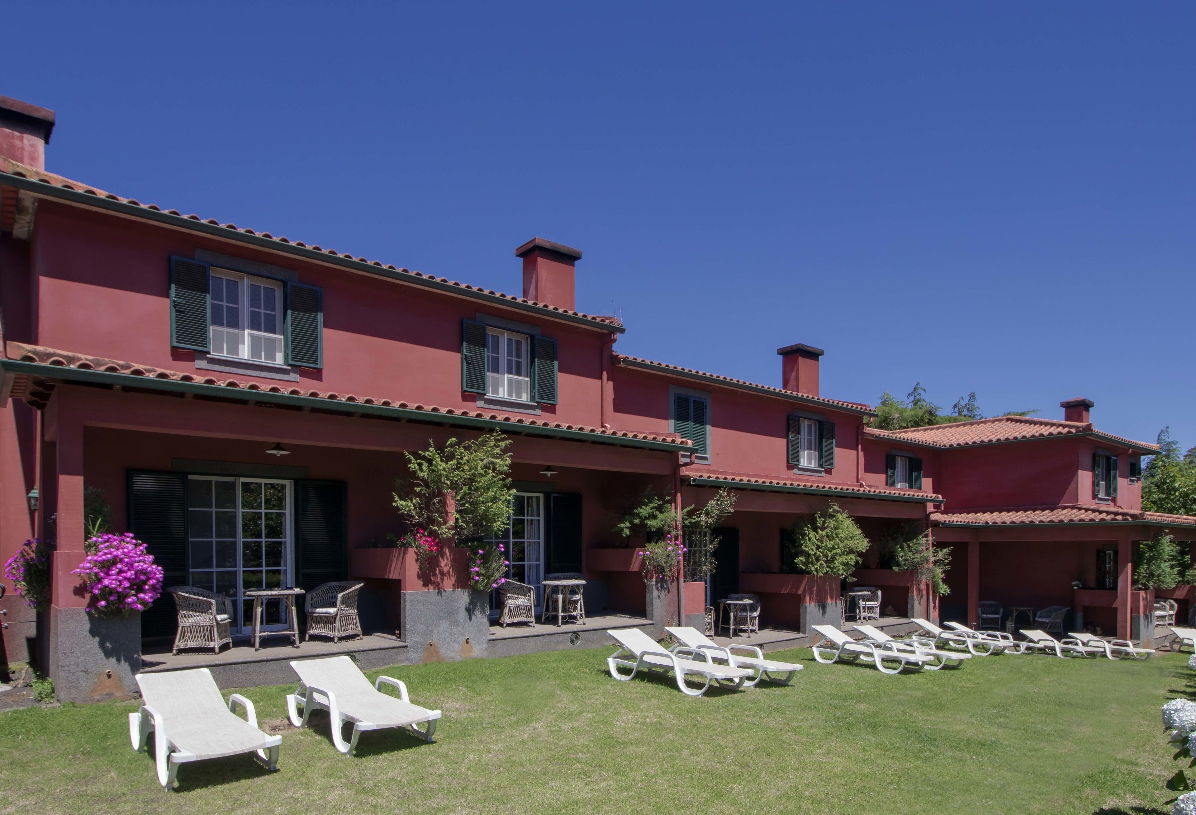 A red building with multiple windows and a covered patio area with lounge chairs and tables.
