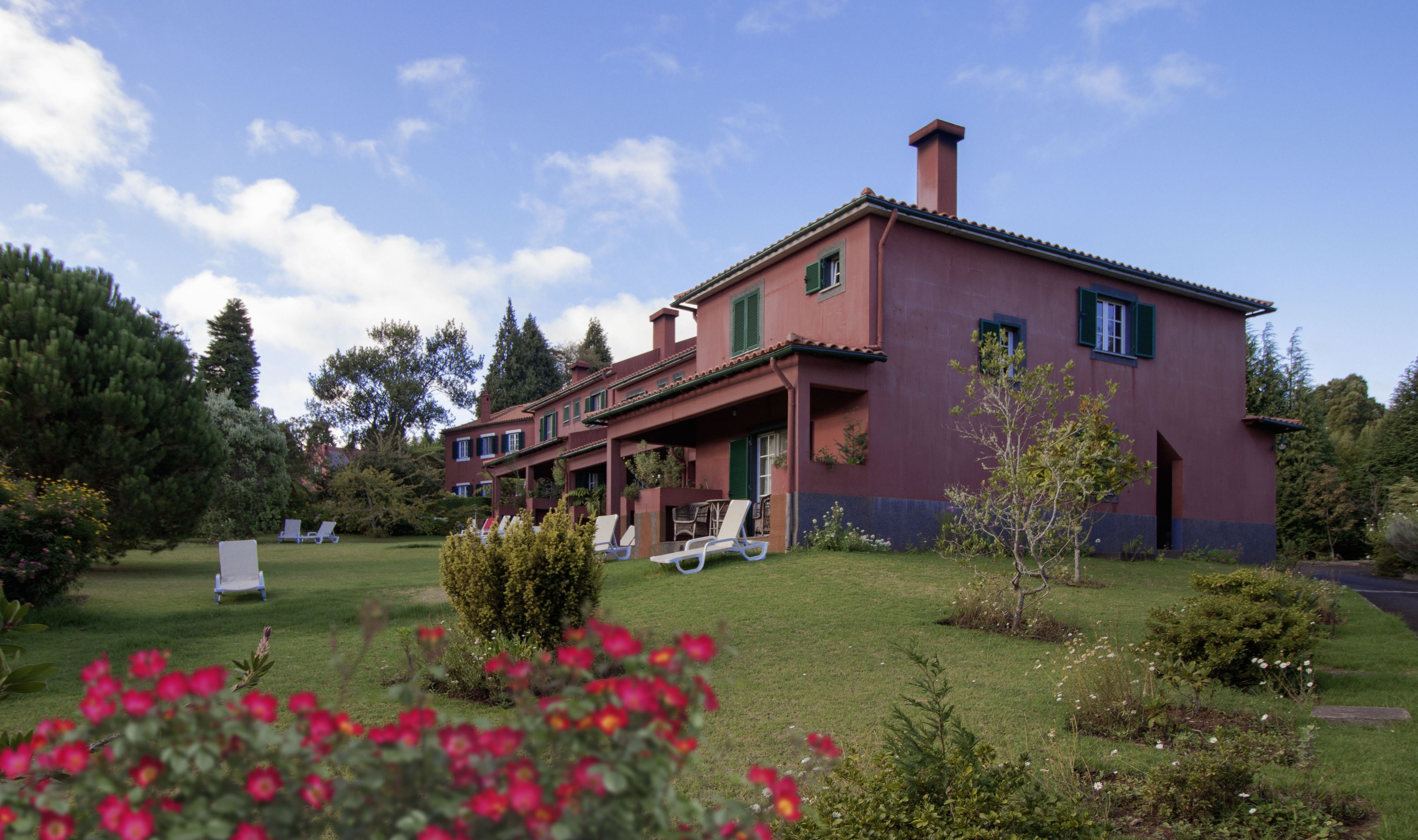 A large, multi-story building with a red facade and green shutters, surrounded by a well-maintained lawn and garden.