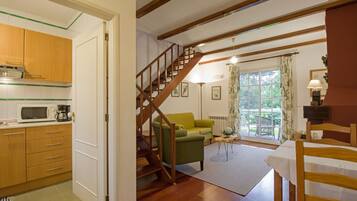 A kitchen with wooden cabinets and a microwave, a staircase leading to a living area with a green sofa, and a dining table with chairs.