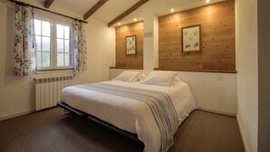 Une chambre avec un grand lit, des poutres apparentes en bois au plafond, un radiateur et deux tableaux encadrés accrochés aux murs.
