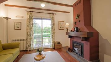 Una sala de estar con chimenea, un sofá, una mesa con un jarrón y una ventana con cortinas.
