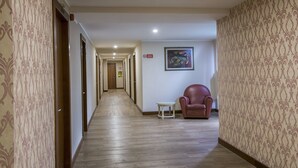 A hotel hallway with patterned wallpaper, a wooden floor, a red armchair, and a small table. - Marchi (Soliera)