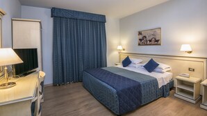 A hotel room with a bed, bedside tables, a desk with a lamp, a television, and a large window with curtains. - Marchi (Soliera)