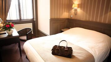 A hotel room with a large bed, a desk with a chair, a lamp, and a vase with flowers.