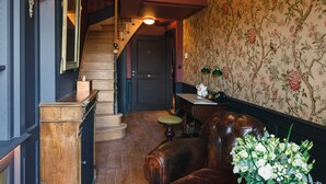 Un intérieur chaleureux avec un escalier en bois, un coin repas avec une table dressée pour deux personnes et un papier peint à motifs floraux.