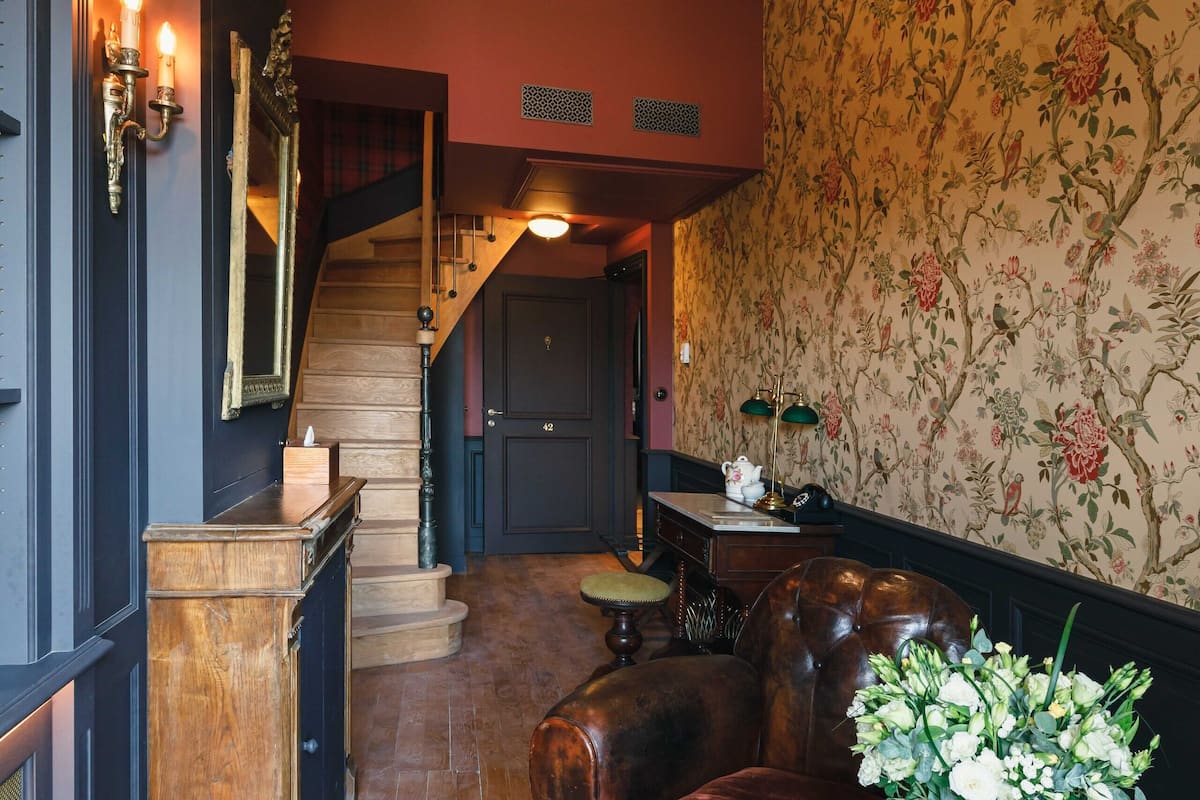 Un intérieur chaleureux avec un escalier en bois, un coin repas avec une table dressée pour deux personnes et un papier peint à motifs floraux.