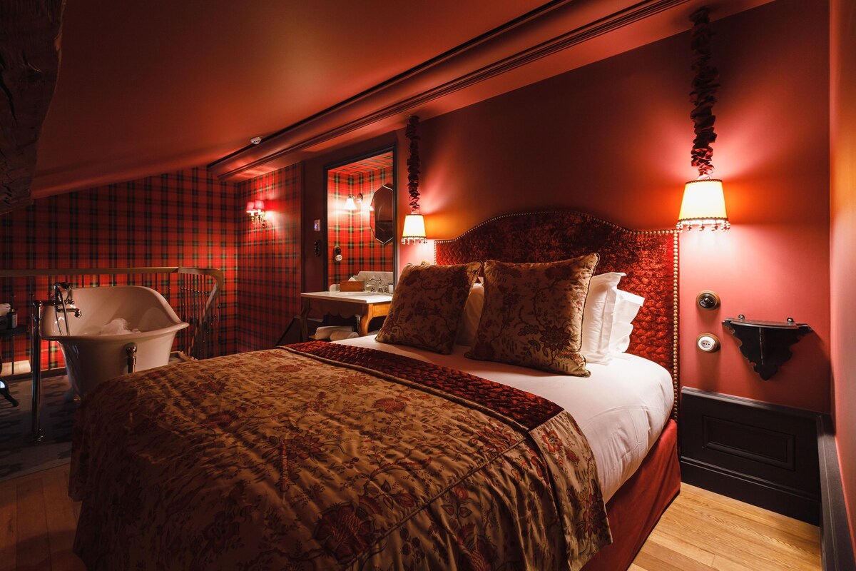 A bedroom with a large bed, a vanity with a mirror, and a bathtub.