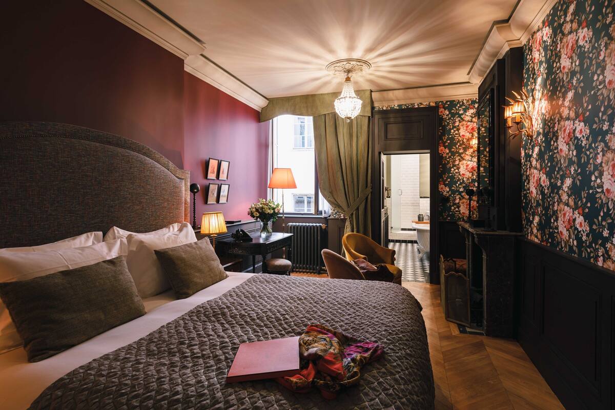 Une chambre avec un grand lit, un bureau avec une lampe, une chaise et une vue sur l’extérieur.