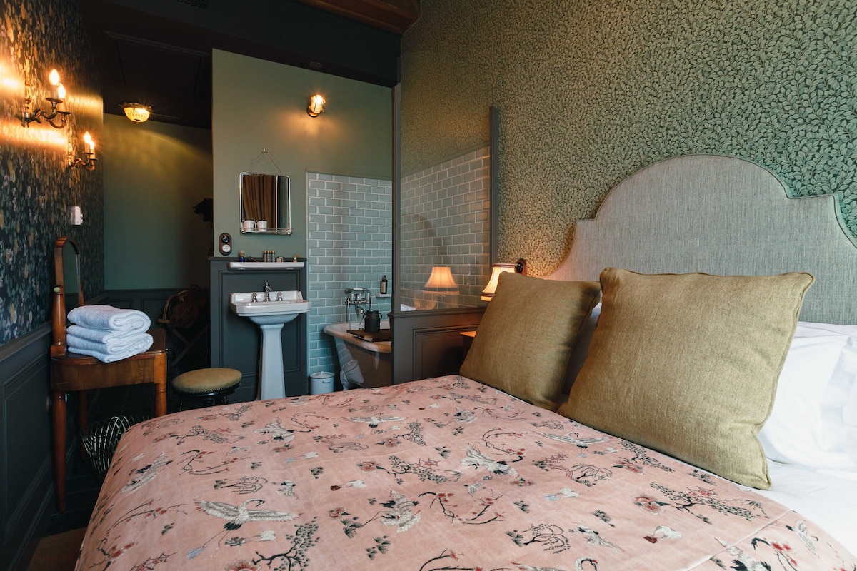 A bedroom with a floral bedspread, a headboard, and a nightstand with a lamp.